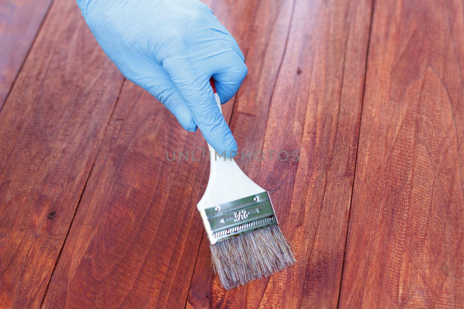 Protective varnishing of a wooden fence in the backyard. Man painting wood stain on wood plank outdoors by lara29