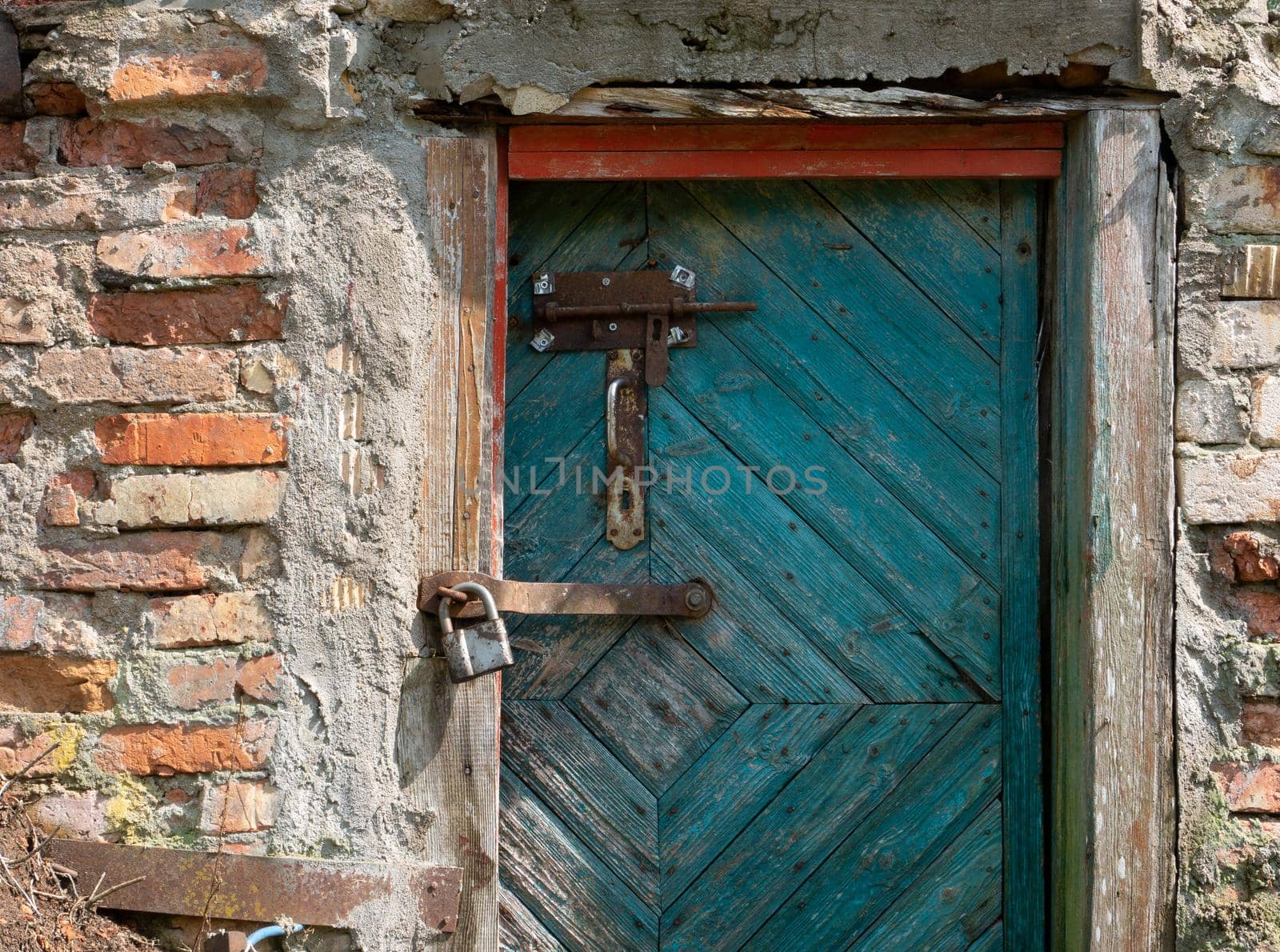 A fragment of an old brick barn with green wooden doors with a metal padlock, bolt and door handle. by gelog67