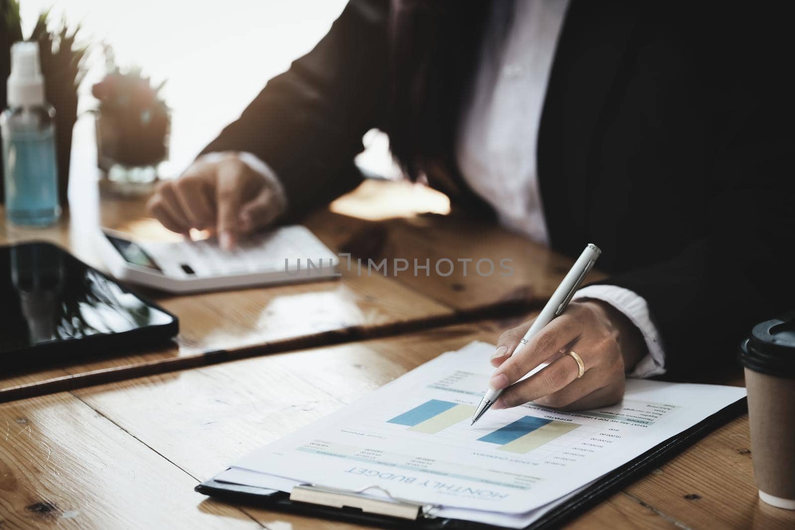 A businesswoman examines financial documents and uses a calculator to research the income affected by the coronavirus pandemic to adjust her marketing strategy. by Manastrong