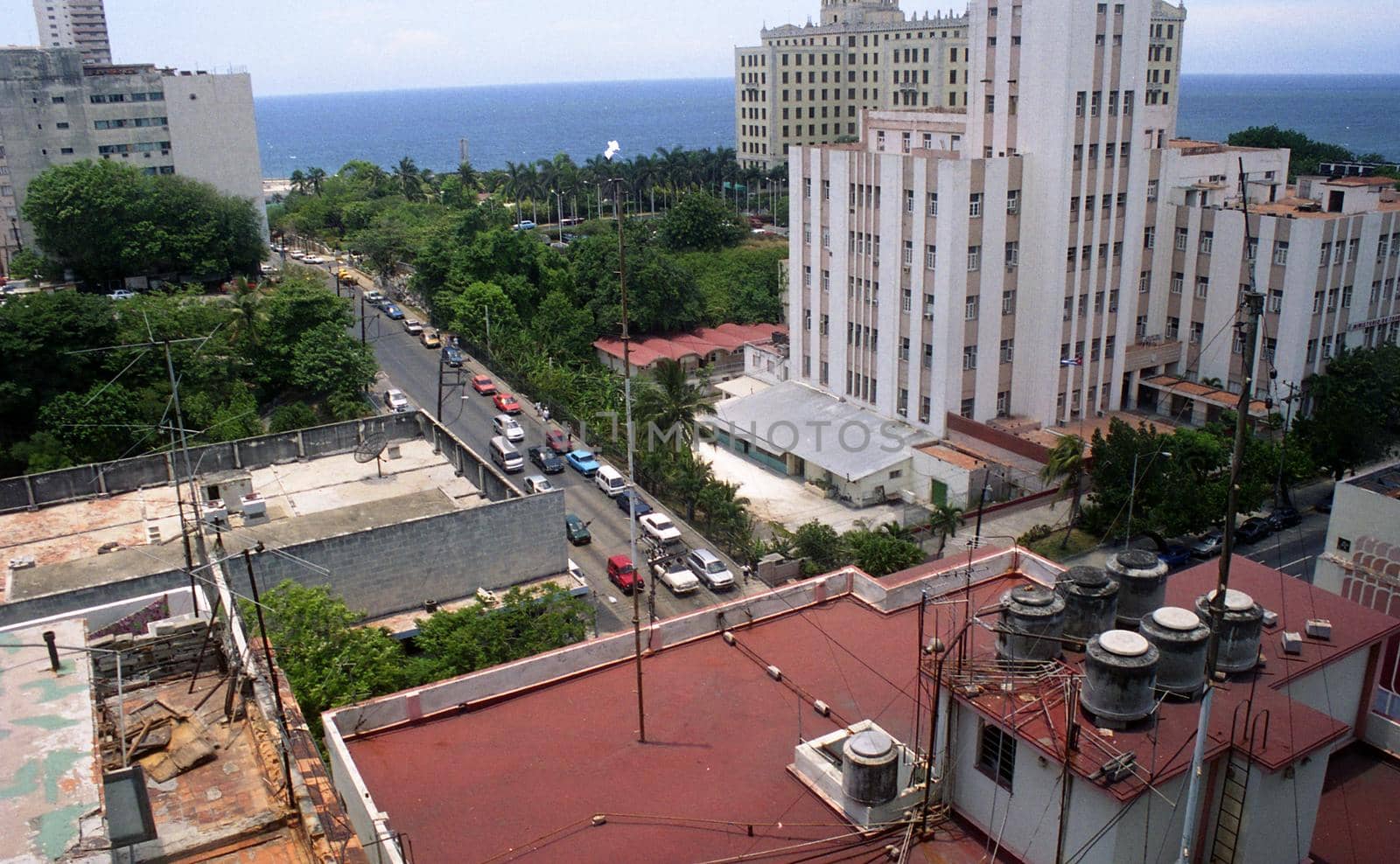 Tall Hotel buildings, Rooftops, and the street below with cars and trees stretching to the water in Havana, Cuba. 2004.