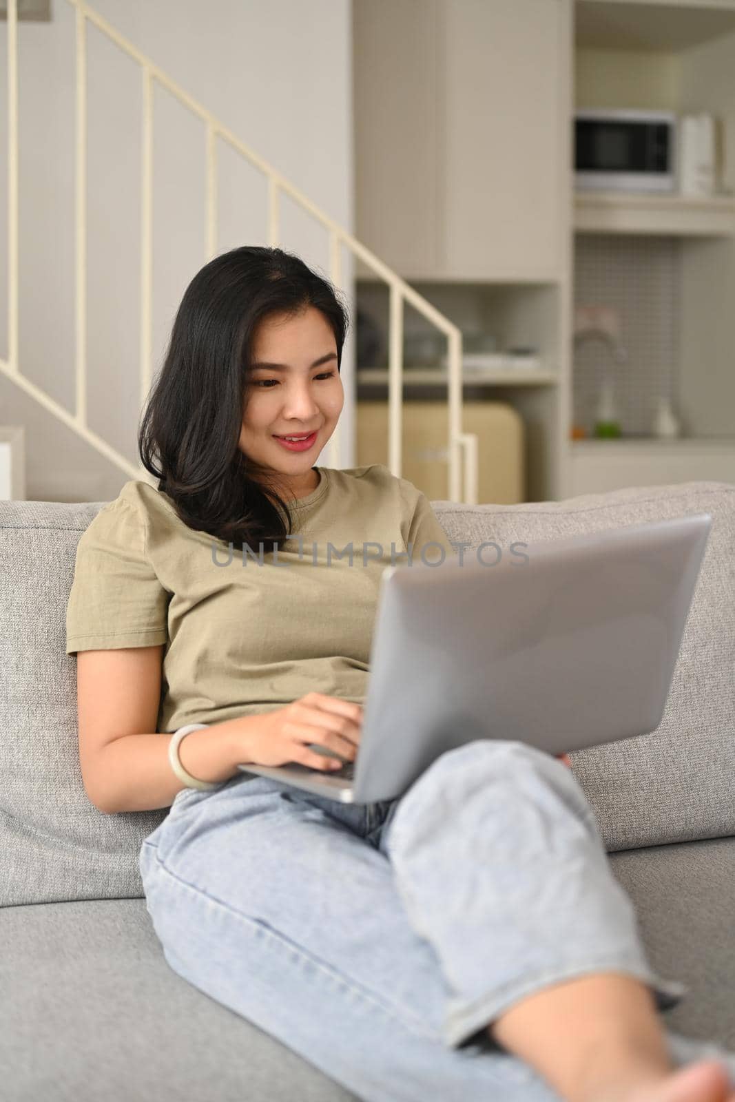 Happy young woman in casual clothes surfing internet on laptop, enjoying leisure weekend time at home.
