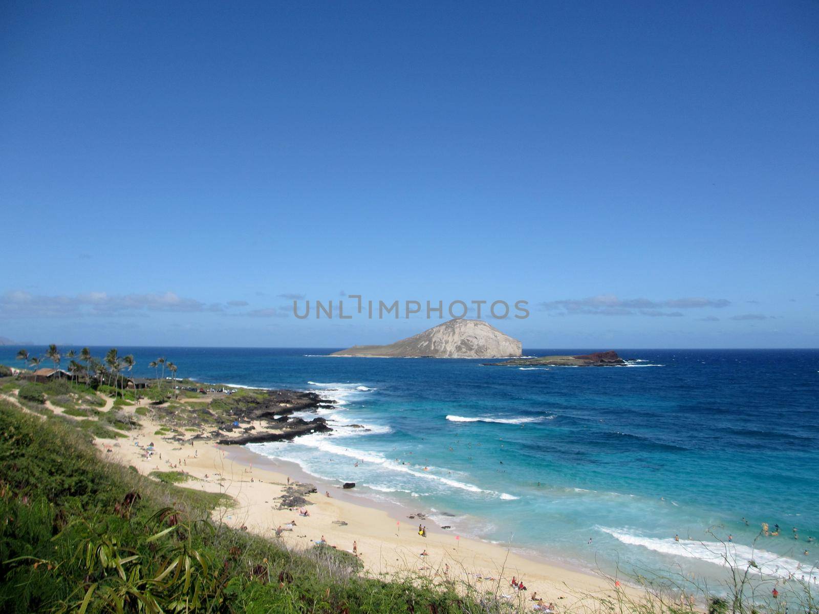 People play at the beach and in surf with view of Rabbit and Rock islands on a clear day at Makapuu Beach Park, Oahu, Hawaii.                              