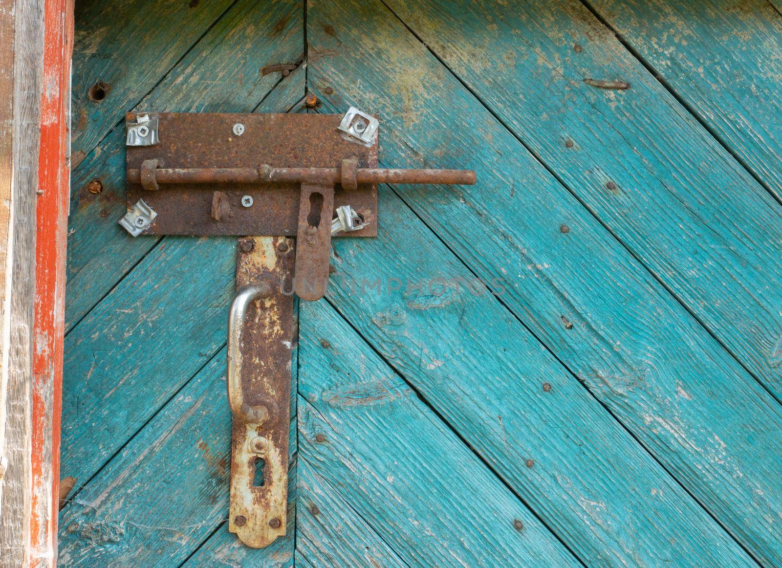 Metal rusty deadbolt and doorknob on old worn green door.