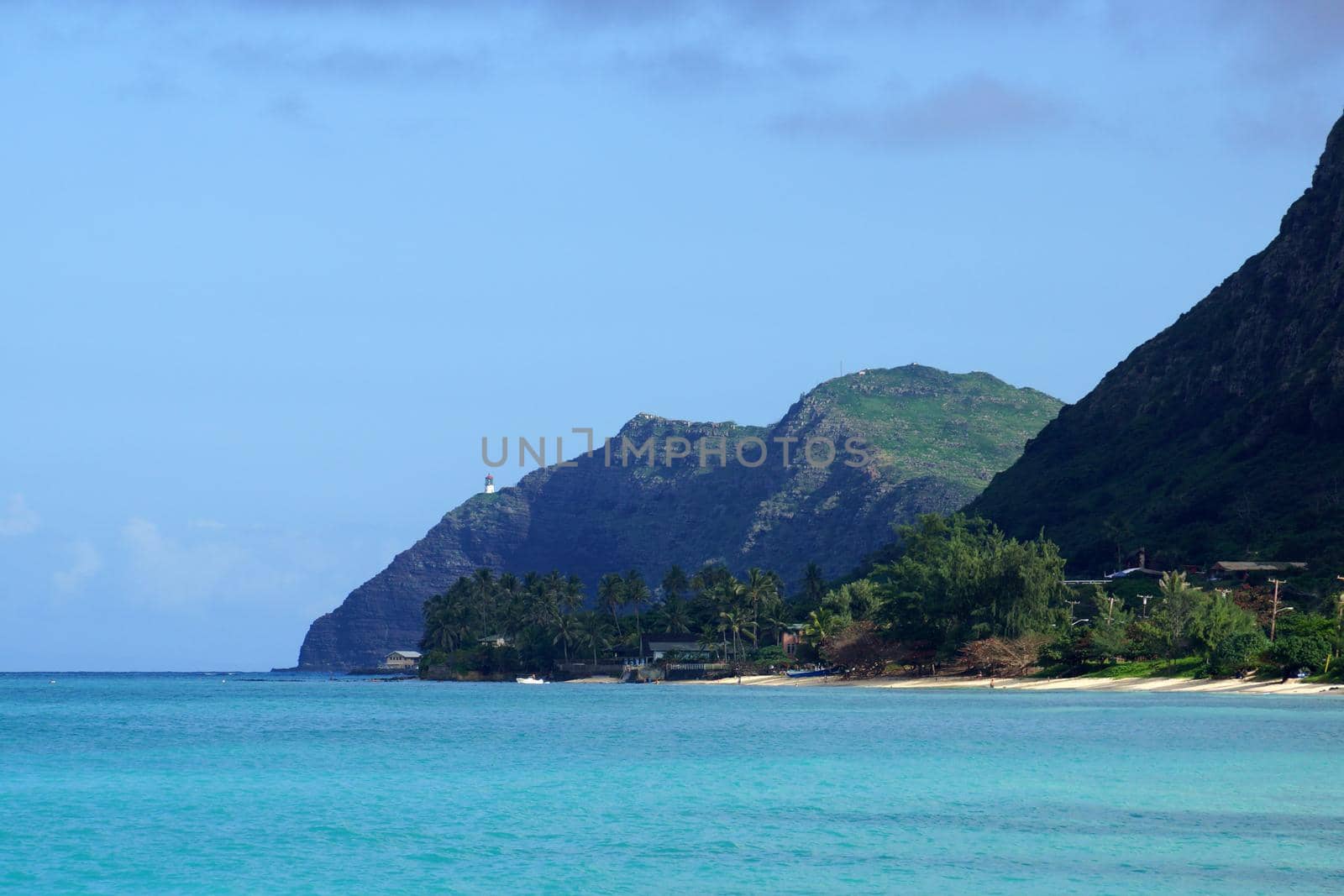 Waimanalo beach, bay, and Makapuu Point with Makapu'u Lighthouse visible on cliffside mountain on windward coast of Oahu, Hawaii and boat in the water.