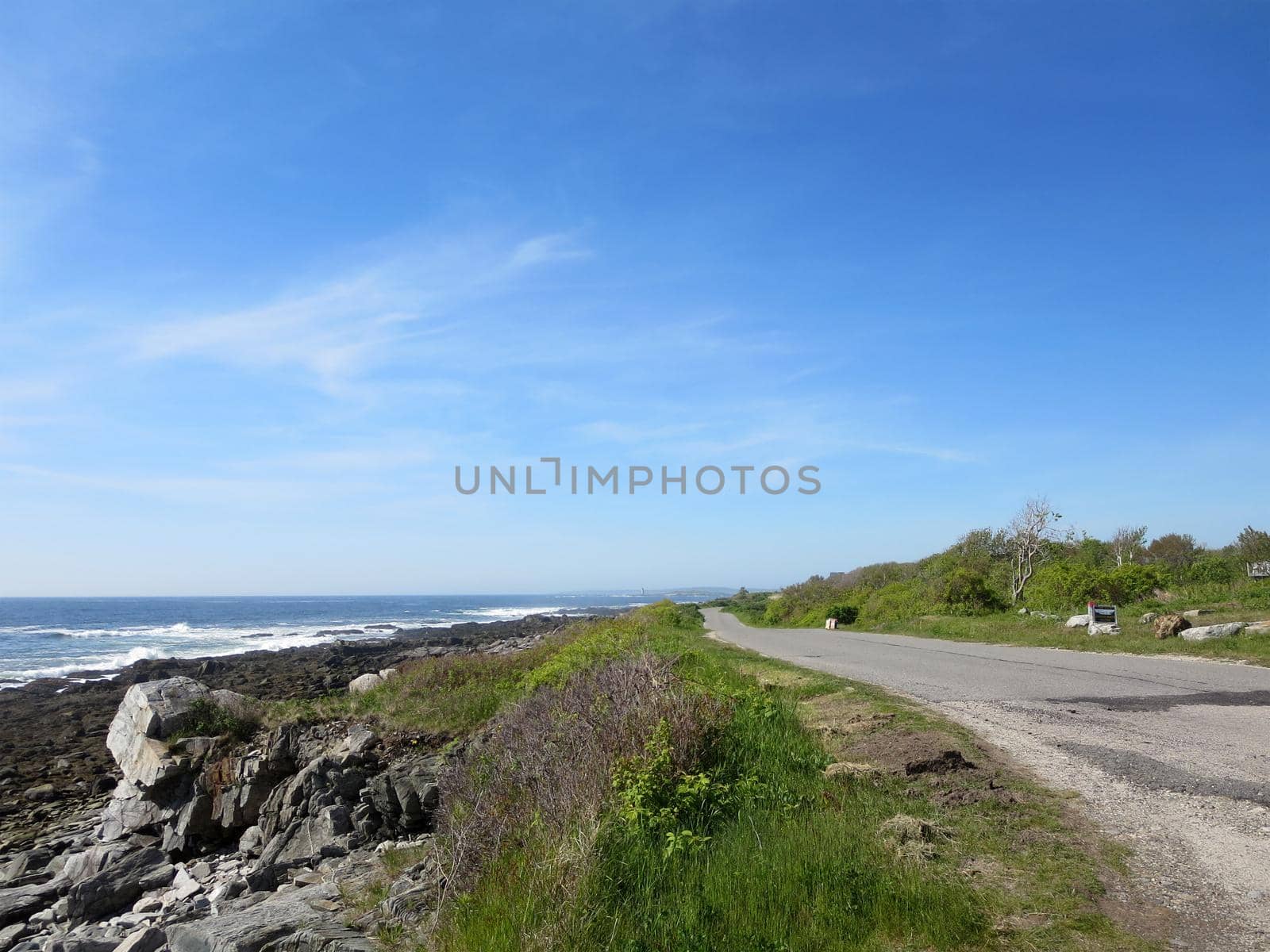 Peaks Island granite rocky Shoreline with road, trees in Maine.