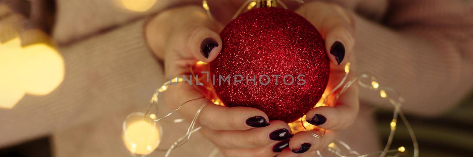 Women's hands in a sweater hold a Christmas ball with garland lights. New year and christmas concept. Copy space, web banner.