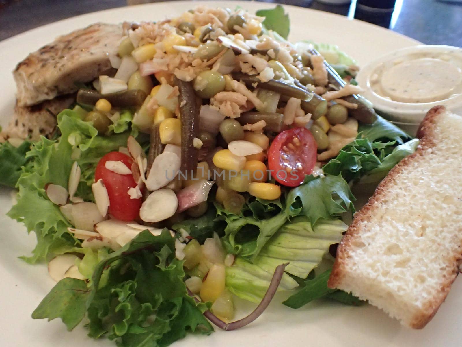 Chicken Salad with spring lettuce, tomatoes, nuts, peas, onions, corn, and bread.  On a white plate with dressing.