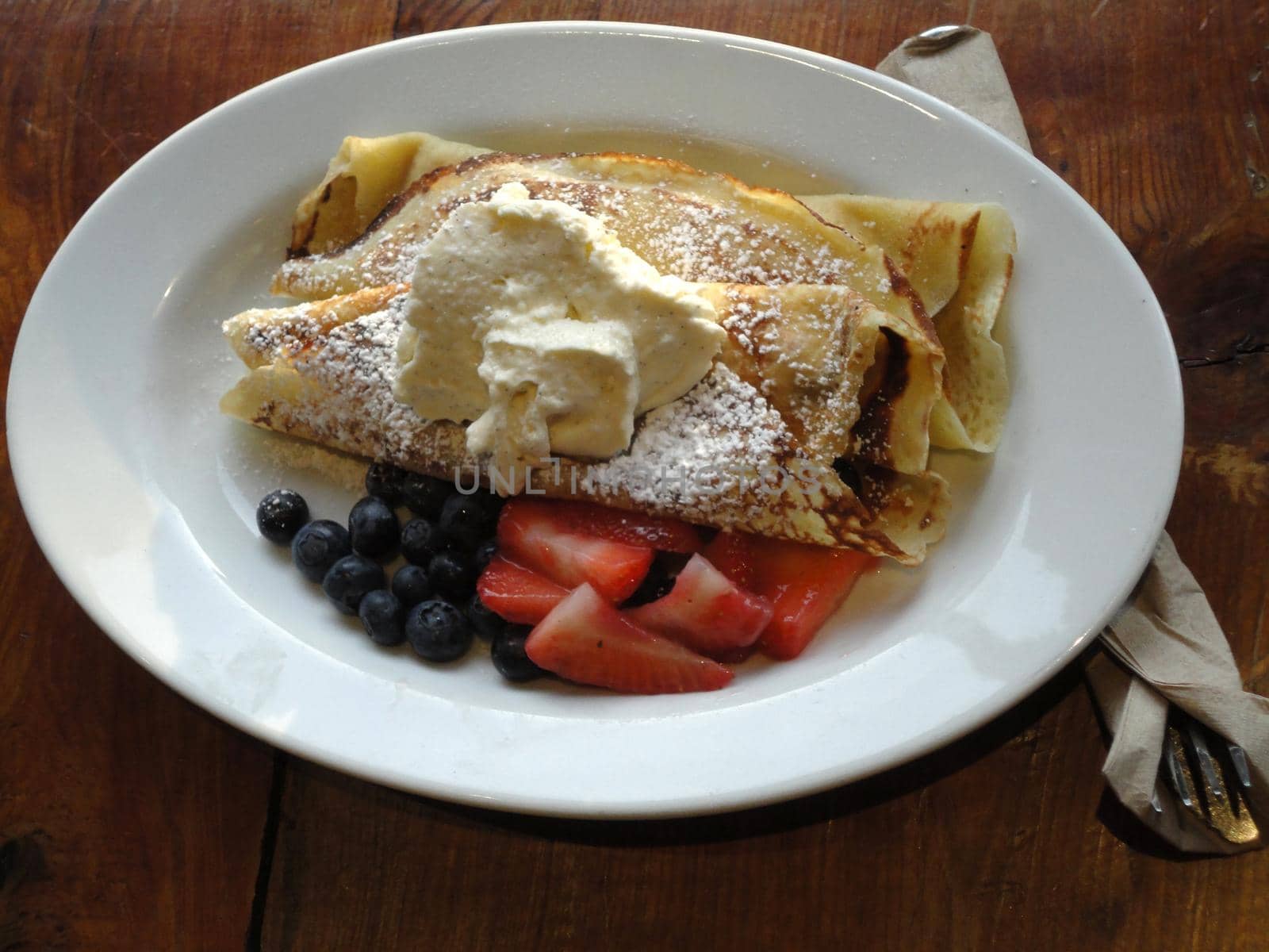 Sweet Crepes Served with sugar ice cream, blueberries and Strawberries on a white plate on a wooden table.