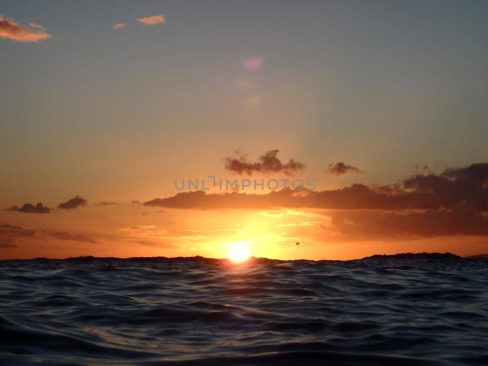 Dramatic lighting the sky and ocean during sunsets with light reflecting on ocean waves moving with parasailer on the water in the distance off Waikiki with clouds on Oahu, Hawaii.