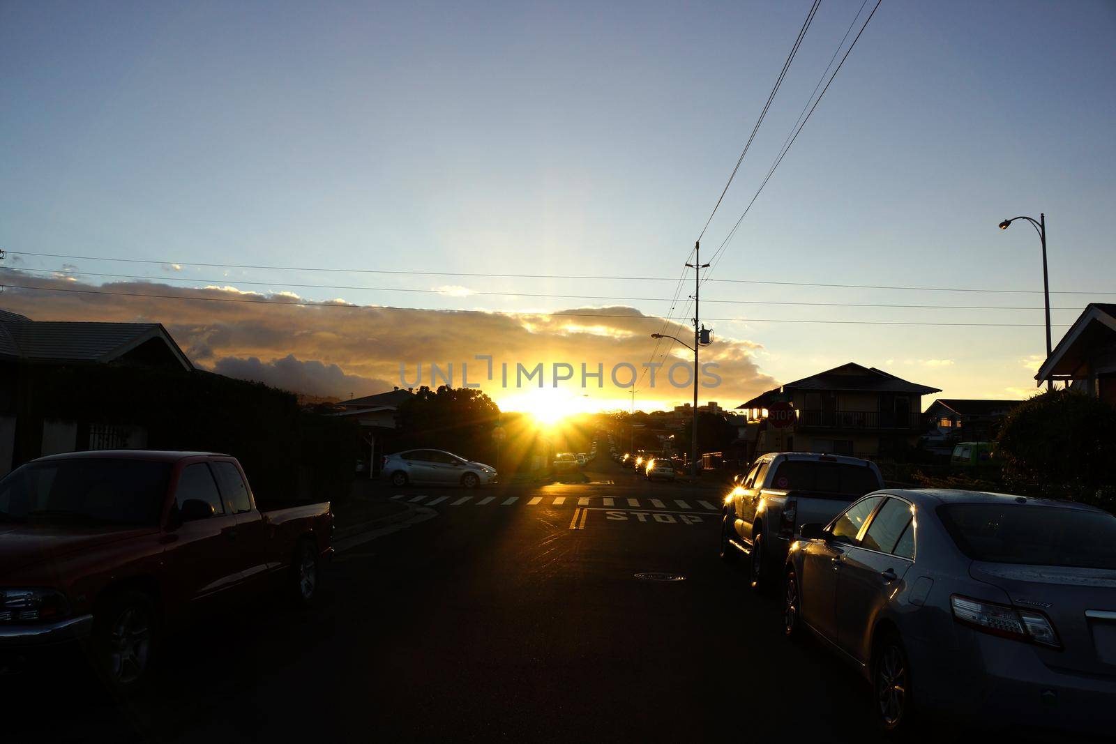 Sunrise over Kapahulu Hill with street lined with cars, power lines, trees and clouds above on Oahu, Hawaii.