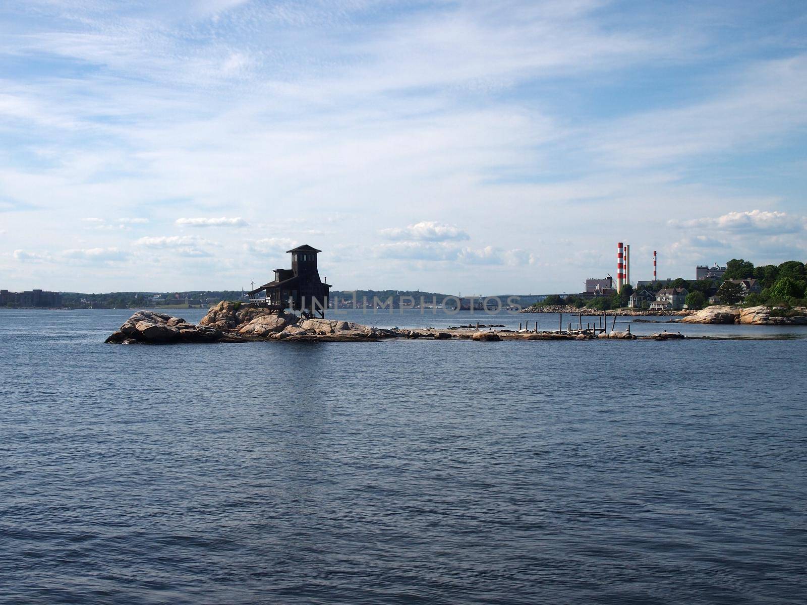 House on Hobs Island in the Thames River as it opens to the sea at Groton Beach looking back towards Connecticut with power plant and homes in the distance.