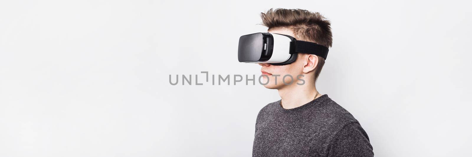 A young guy, a teenager stands in a villard vr glasses on a white background. Augmented reality in our time. A virtual reality glasses boy plays games and learns at school. Web banner