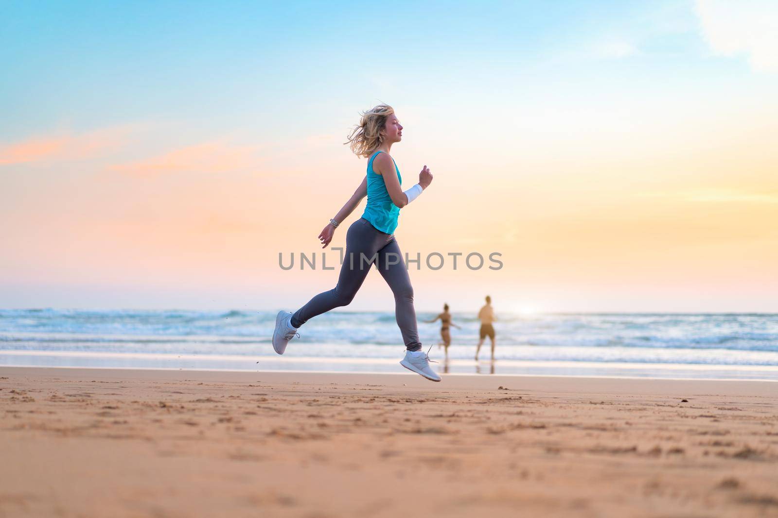 Active sporty woman run along ocean surf by water pool to keep fit and health. Sunset sand beach background with sun. Woman fitness, jogging workout and sport activity on summer family holiday.