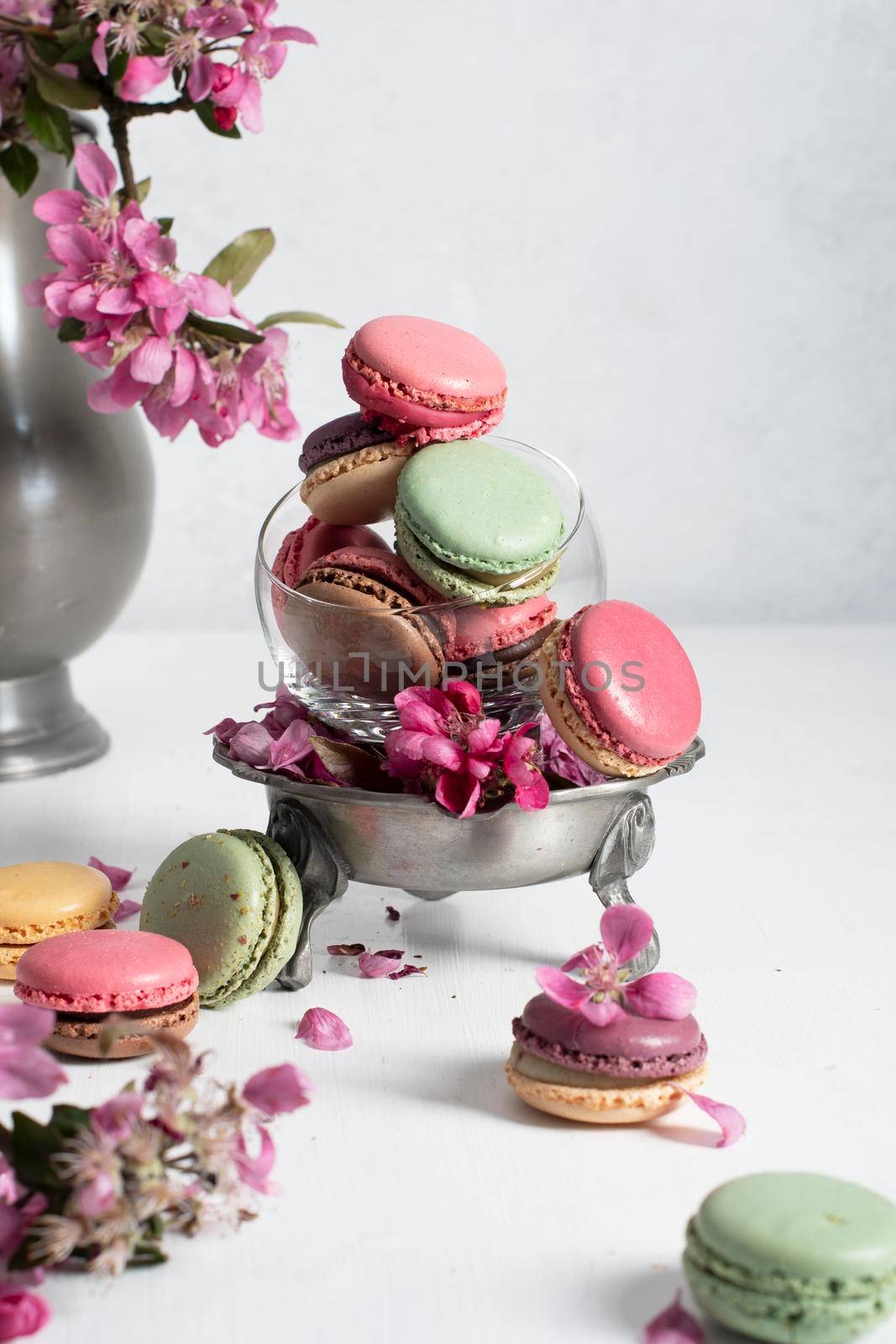 spring still life with colored macaroons and pink apple tree flowers in a pewter vase, colorful sweet food close up. High quality photo
