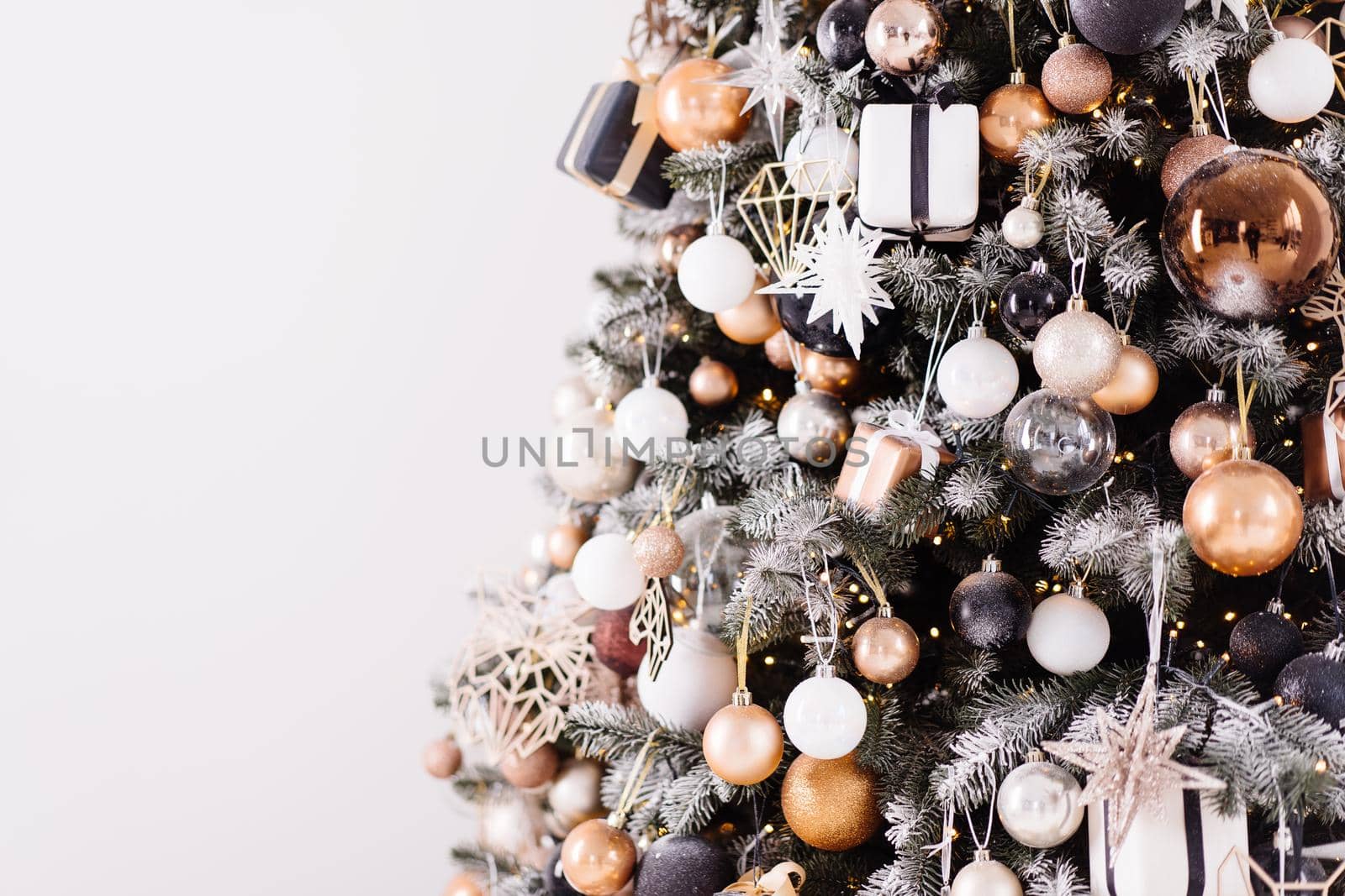 Christmas tree close up standing white wall background decorated white black gold color with light garland. Christmas decoration with copy space