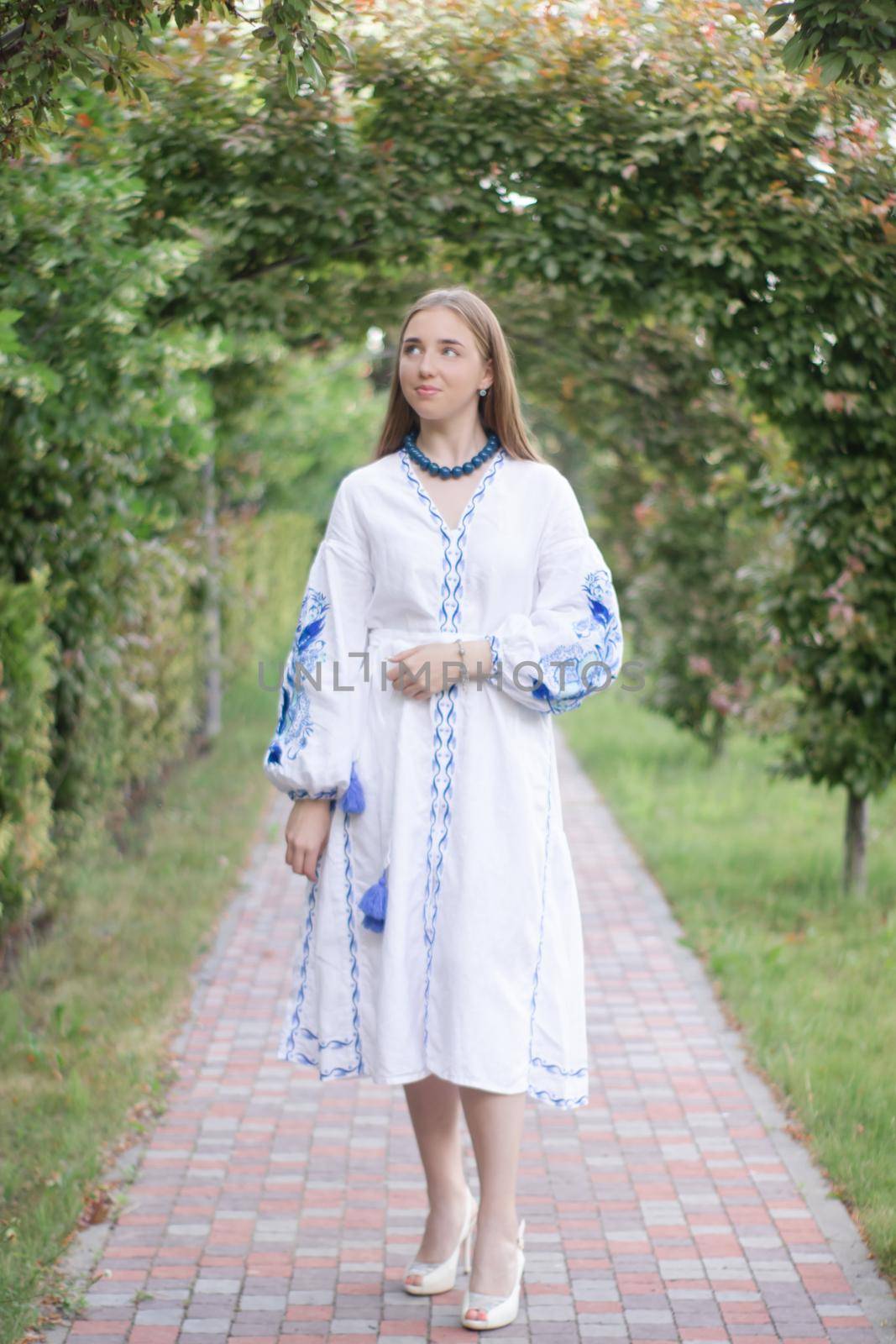 Portrait of young Ukrainian woman dressed in blue national traditional embroidered shirt in park outdoor.