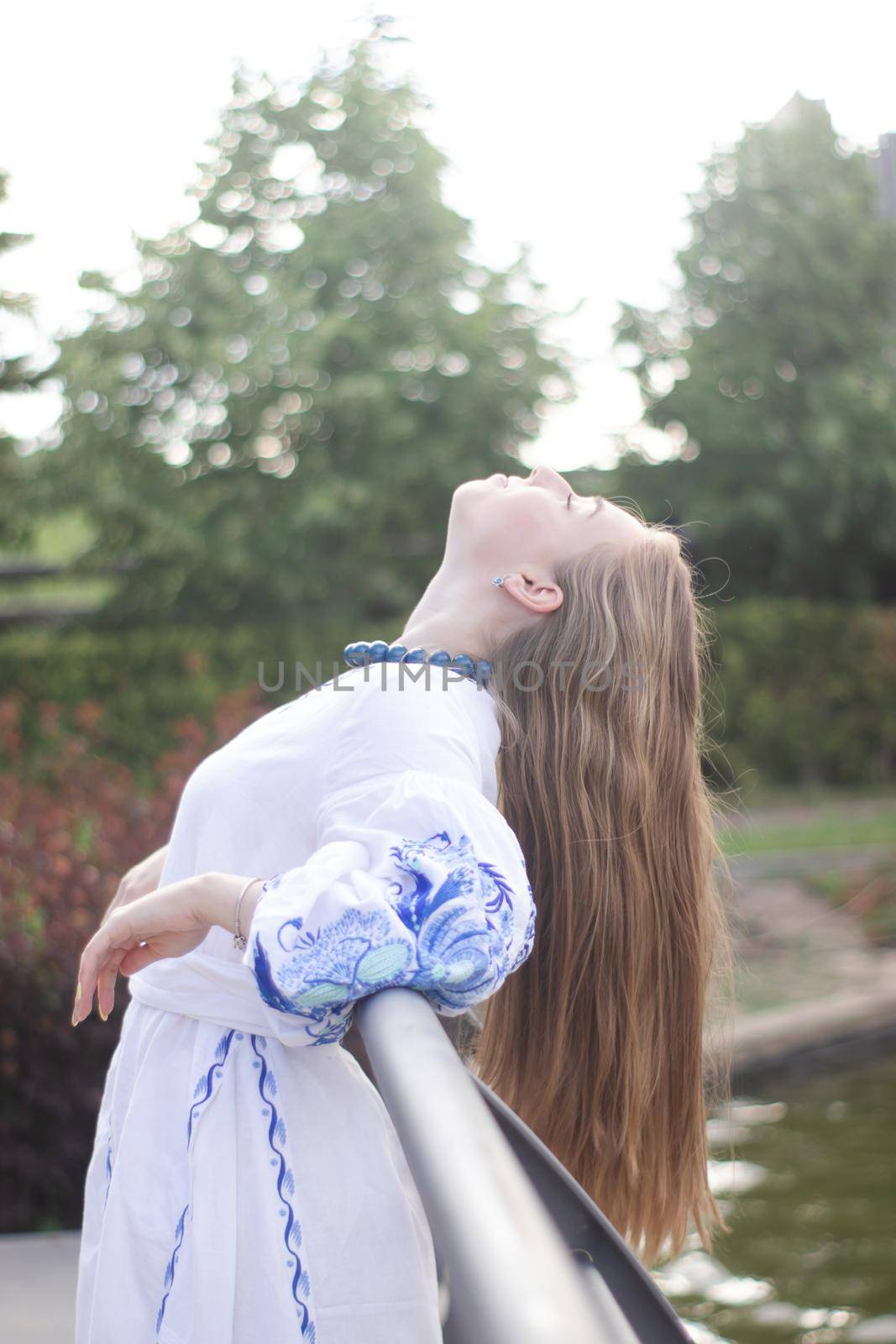 Portrait of young Ukrainian woman dressed in blue national traditional embroidered shirt in park outdoor.