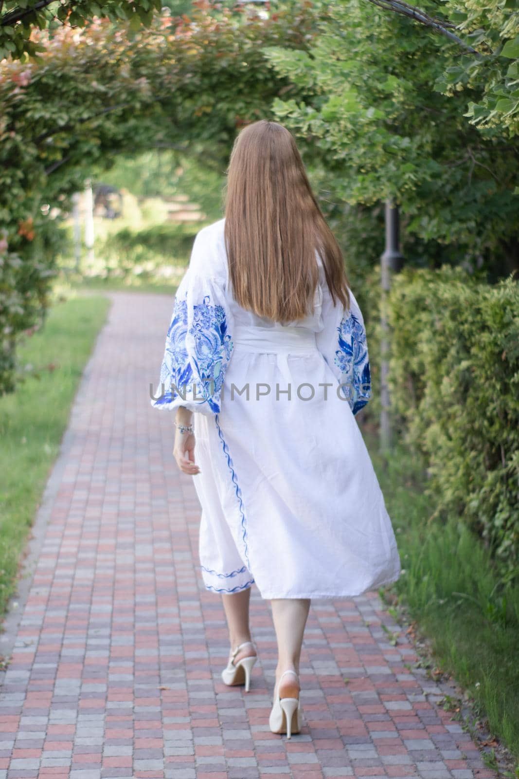 Portrait of young Ukrainian woman dressed in blue national traditional embroidered shirt in park outdoor.