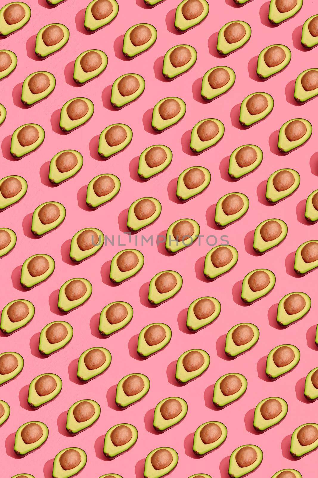 Food design. Top view of colorful fruit pattern of fresh cutted avocado halves with pits inside on coral pink pastel background. Mock up, flat lay style.