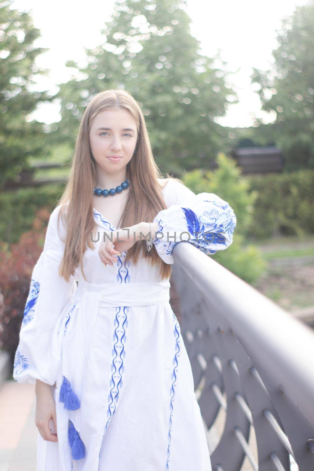 Portrait of young Ukrainian woman dressed in blue national traditional embroidered shirt in park outdoor by oliavesna