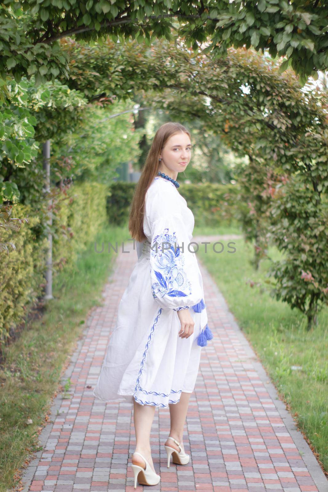 Portrait of young Ukrainian woman dressed in blue national traditional embroidered shirt in park outdoor.