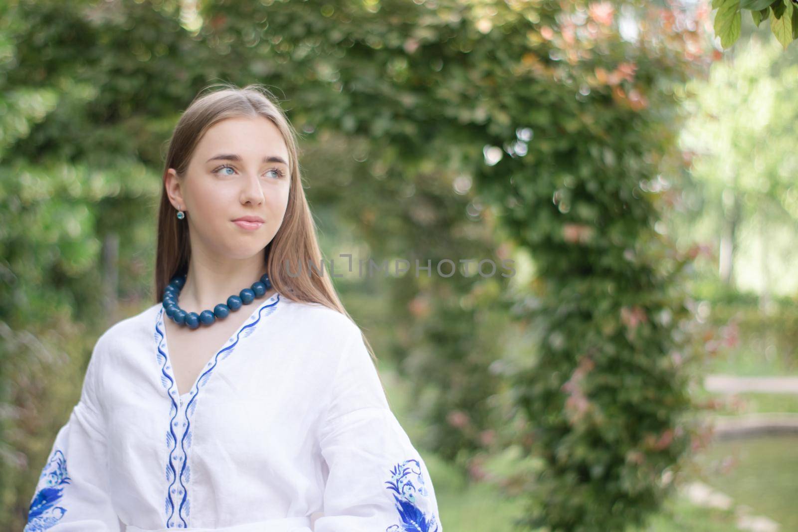 Portrait of young Ukrainian woman dressed in blue national traditional embroidered shirt in park outdoor.