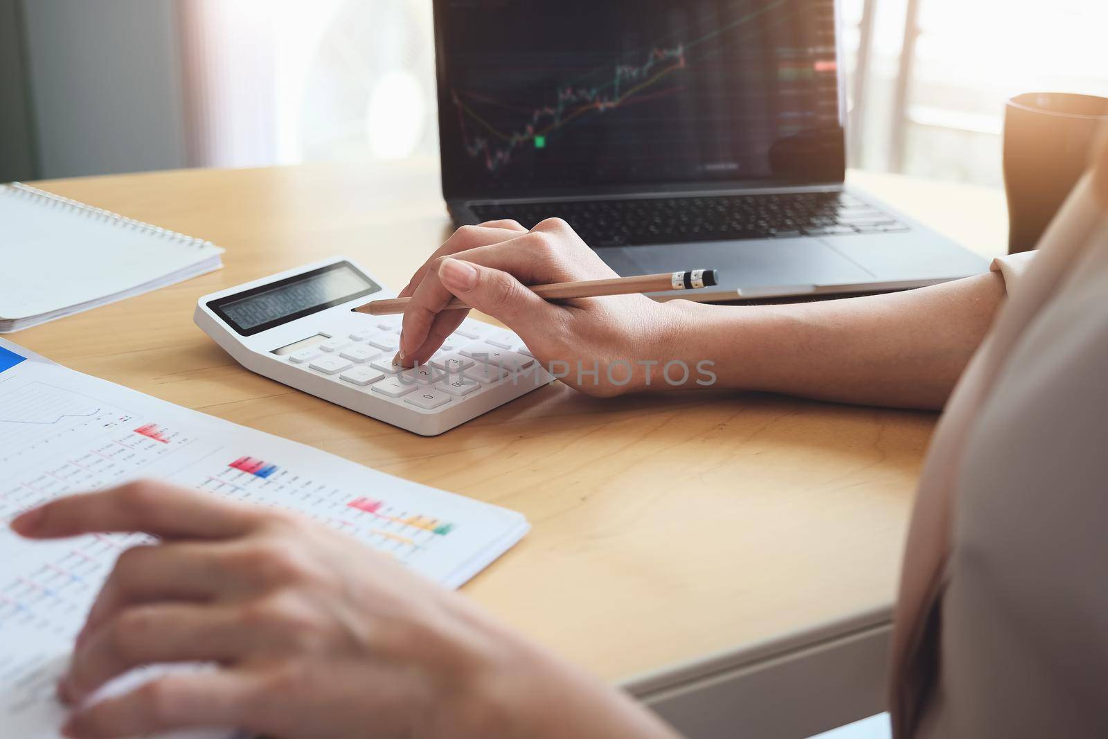 Business woman using calculator and computer to trade charts to find buy and sell points for her port by Manastrong