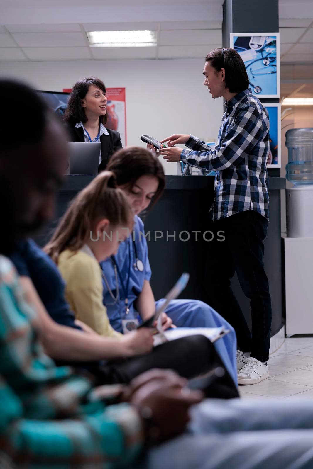 Asian patient at hospital front desk paying at pos using credit card for medical services by DCStudio