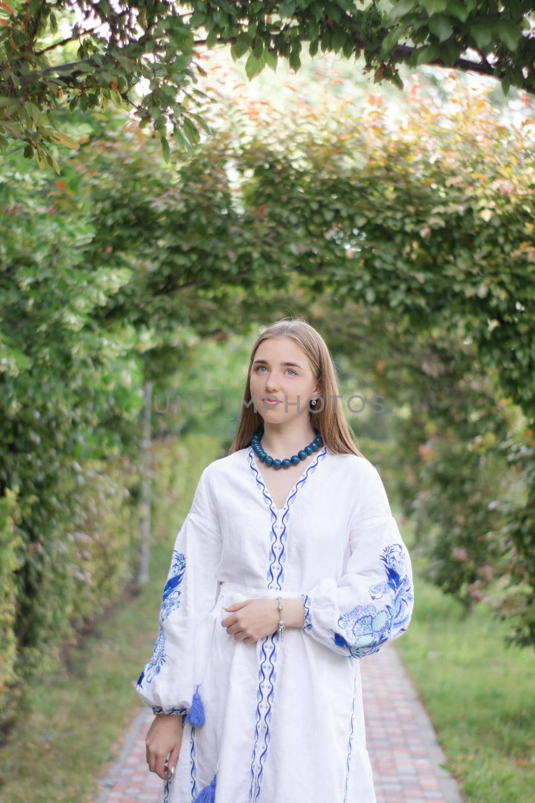 Portrait of young Ukrainian woman dressed in blue national traditional embroidered shirt in park outdoor by oliavesna