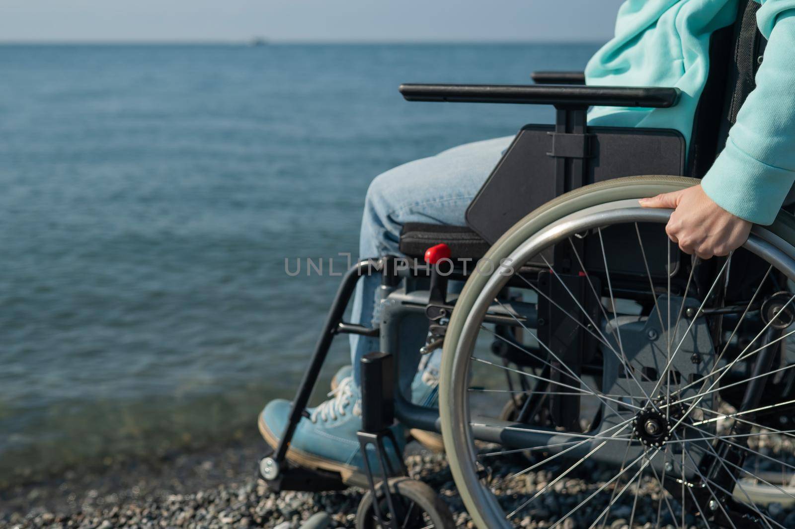 Caucasian woman in a wheelchair on the seashore. Close-up of female hands