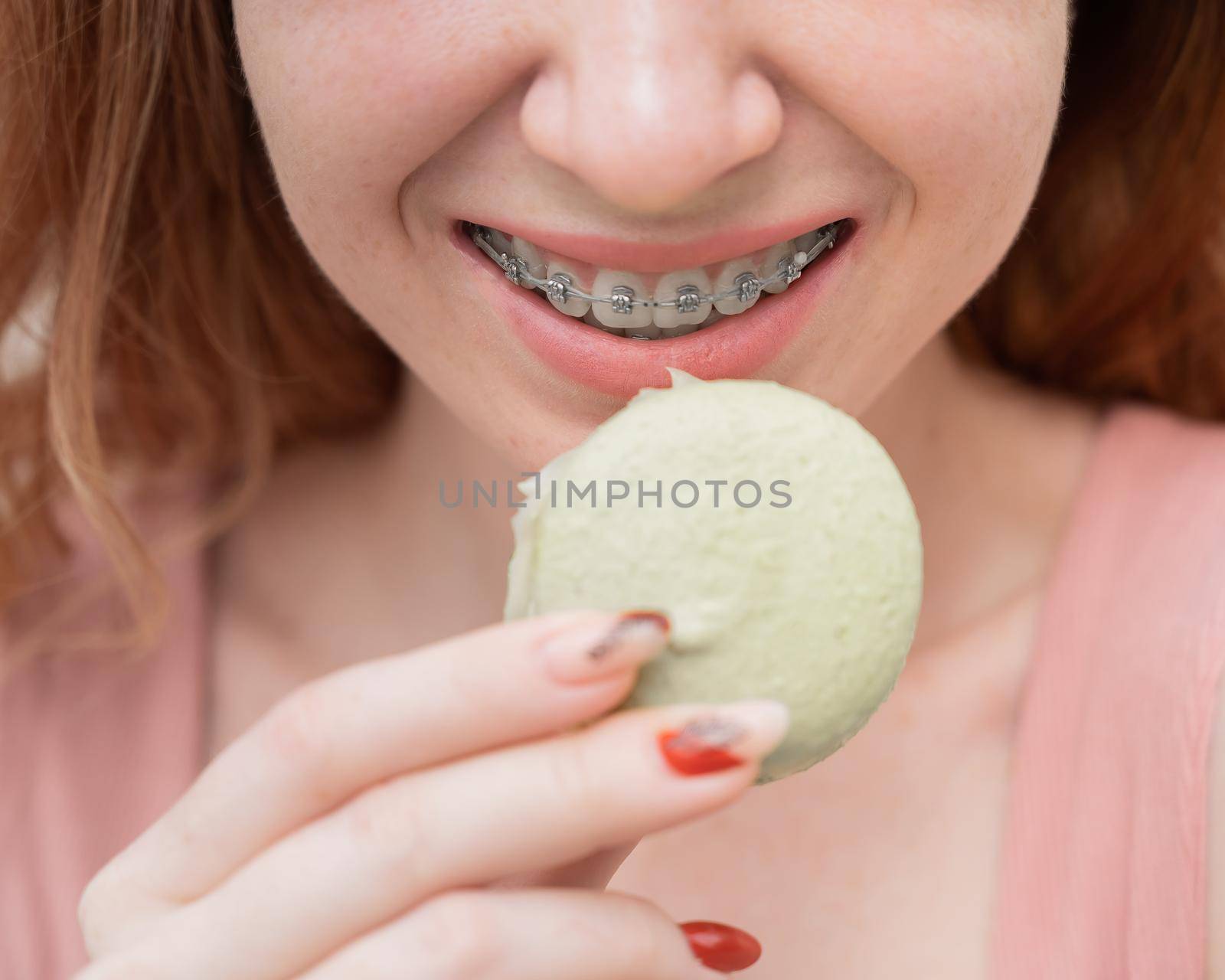 Young red-haired woman with braces eating macaron cake