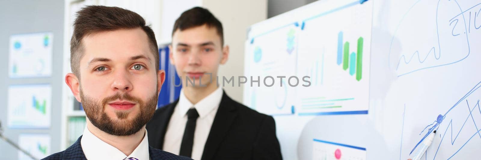 Portrait of smart people demonstrate some graphics and charts on white board. Attractive manager in classy suit and striped tie. Report, conference concept