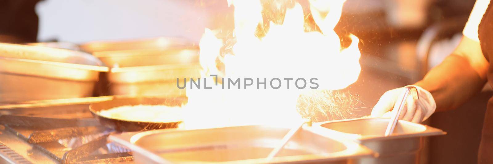 Close-up of chef cooking something delicious on stove, burning flame from dish. Impressive show for visitors on open air. Cooking, cafe, takeaway concept