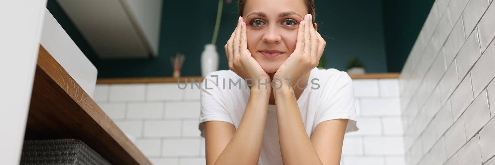 Low angle of smiling young woman sitting on toilet seat, comfort restroom at home, female went to pee. Bathroom, nature calls, renovation, interior concept