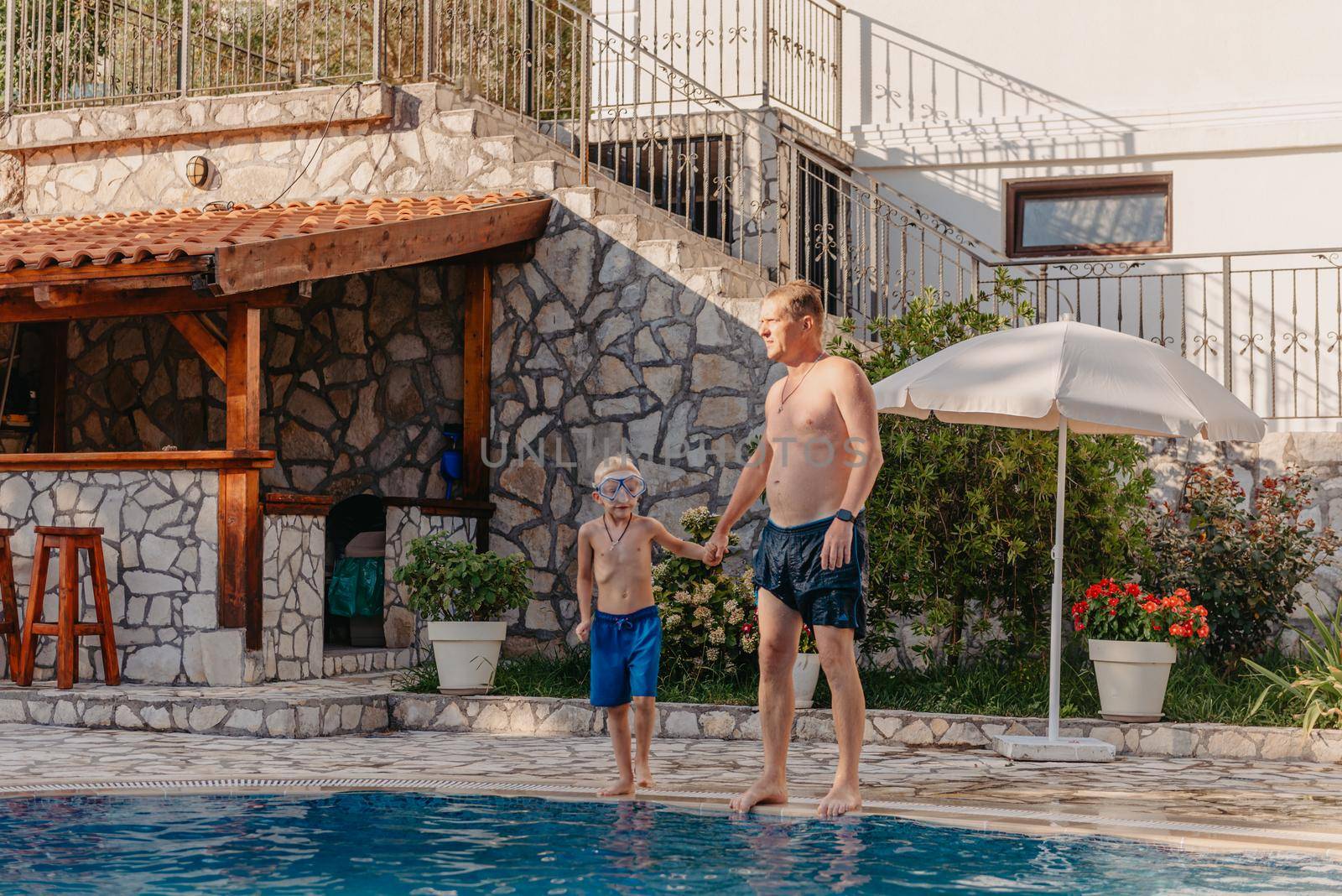 Excited boy in googles jumping in water from shoulders of his father standing in swimming pool