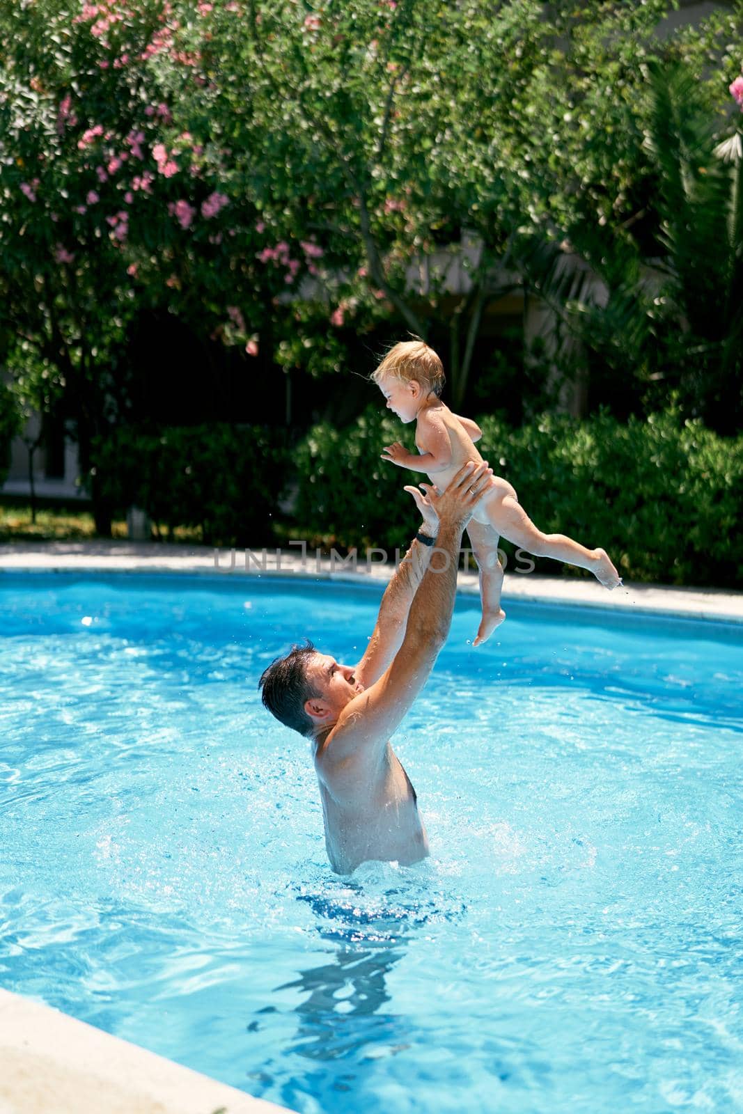 Dad throws a small child in the air over the water in the pool. High quality photo