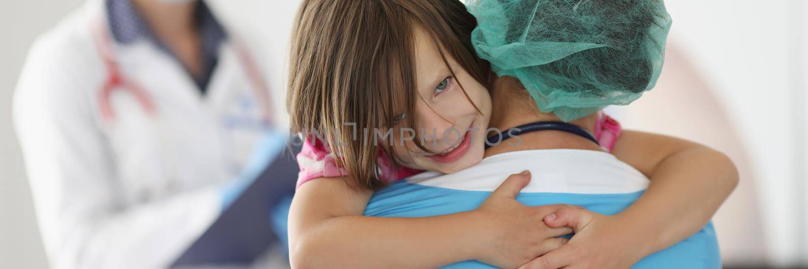 Portrait of little girl climbed on hands to medical worker to thank for help. Cheerful kid feel relaxed and happy in clinic. Childhood, medicine concept