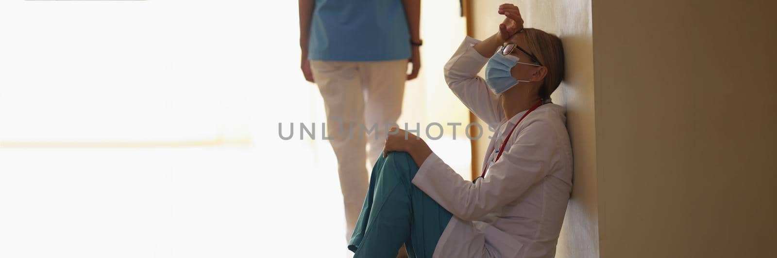 Low angle of female surgeon exhale after long operation sitting in clinic corridor on floor. Deserved rest after hard operation. Health, save life concept