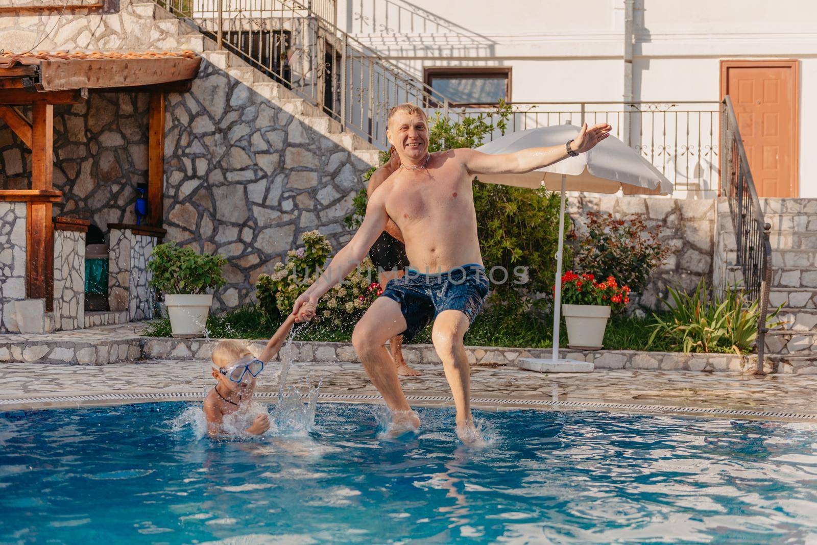 Excited boy in googles jumping in water from shoulders of his father standing in swimming pool by Andrii_Ko