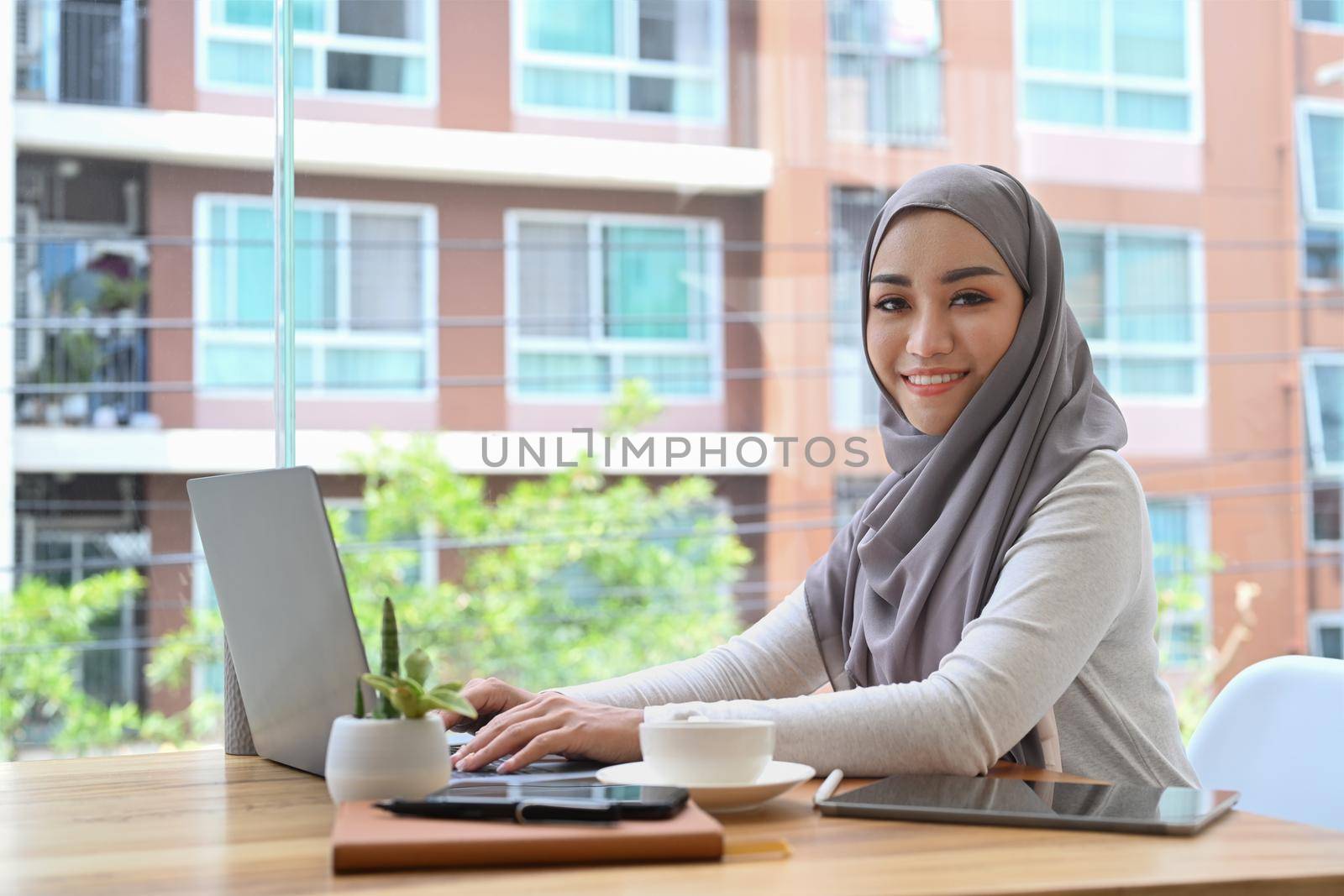 Elegant Muslim woman wearing hijab using computer laptop in her personal office.