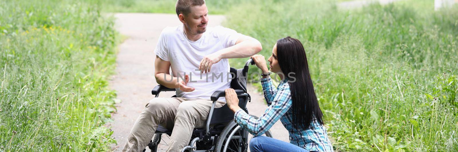 Portrait of young woman comforting husband in wheelchair, support in recovery. Walk on fresh air in park. Healthcare, family, relationship, support concept