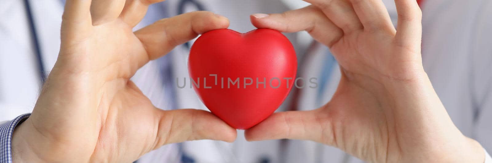 Close-up of medical workers colleagues together hold plastic red heart. Save life through donation or charity. Medicine, cardiology, healthcare concept