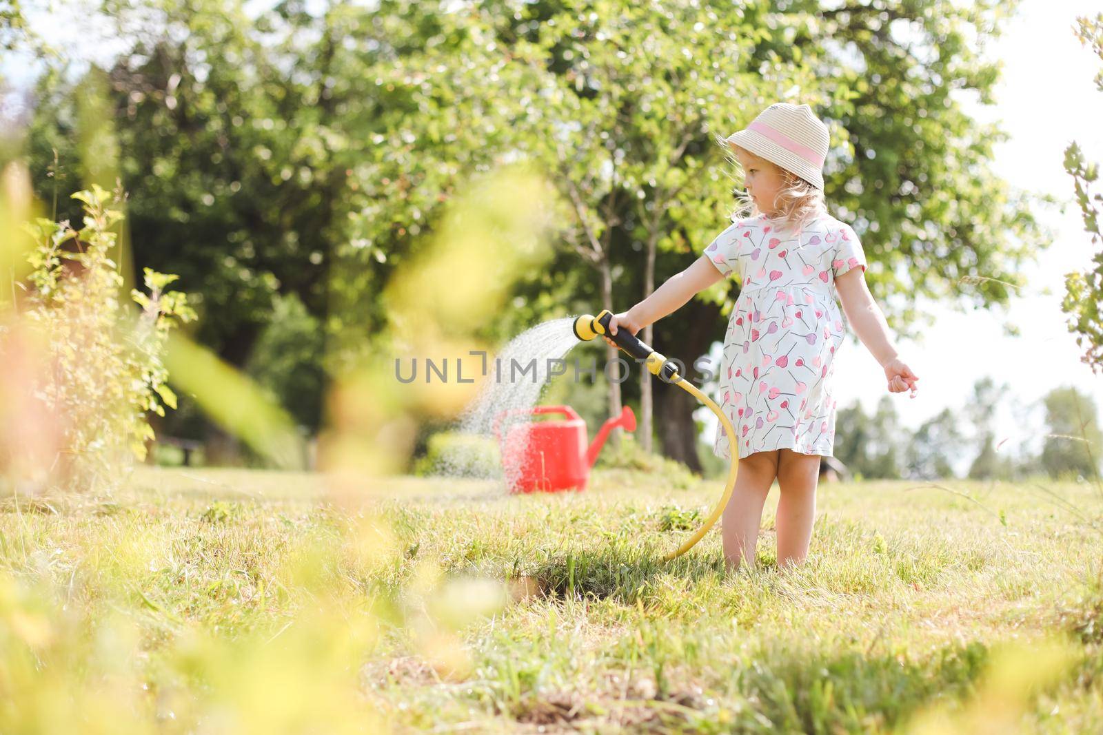 Adorable little girl playing with a garden hose on hot sunny summer day