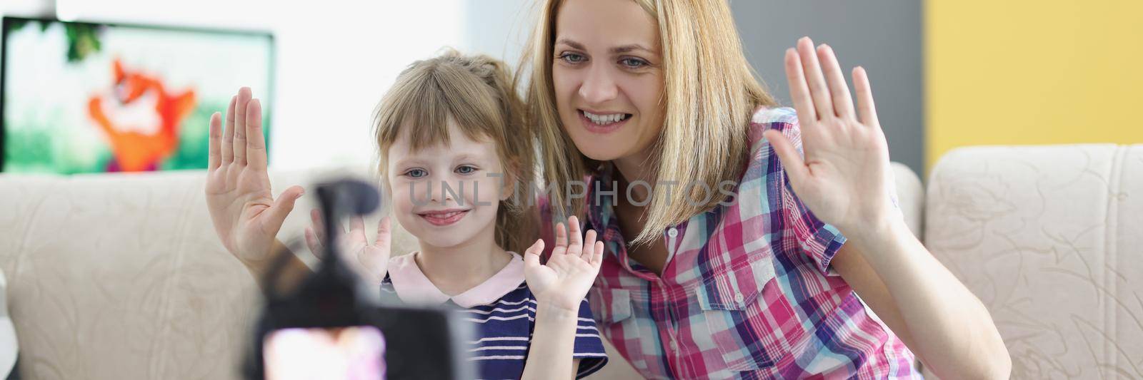 Mother and daughter wave hello on video, videocamera set on tripod by kuprevich