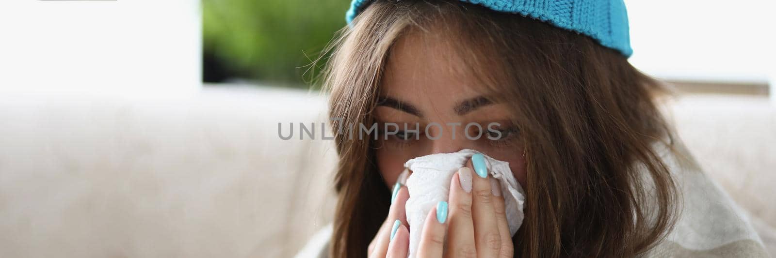 Portrait of woman wipe wet running nose with tissue dressed in warm hat and covered with blanket. Stay on self isolation, recover at home. Sickness concept