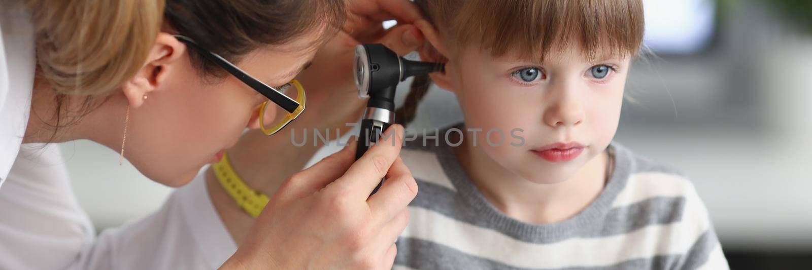 Portrait of little girl sit calm while family doctor examine ears with special equipment. Girl not afraid of doctors and clinic atmosphere. Health concept