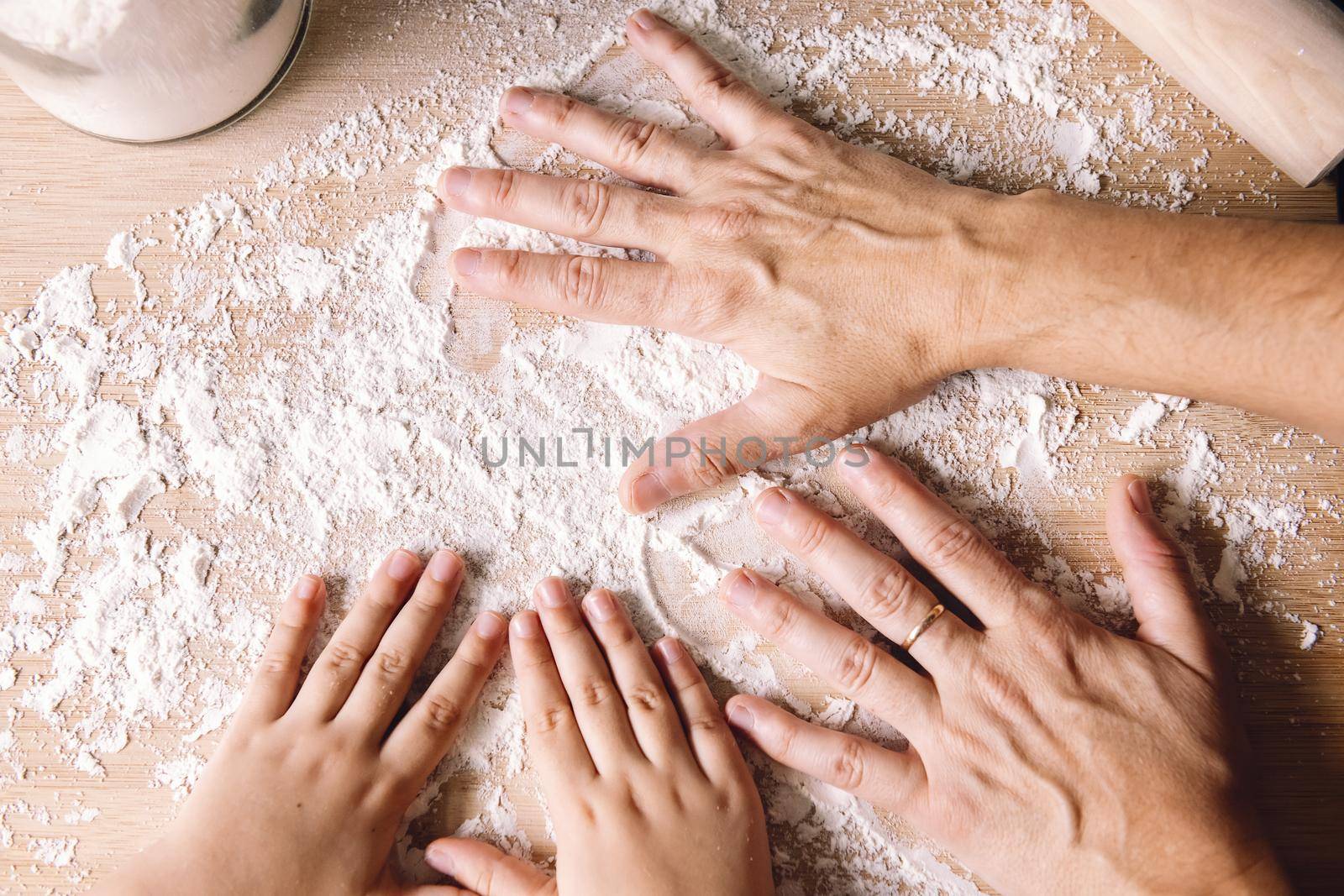 mother and daughter hands putting flour on the kitchen table, concept of healthy food at home