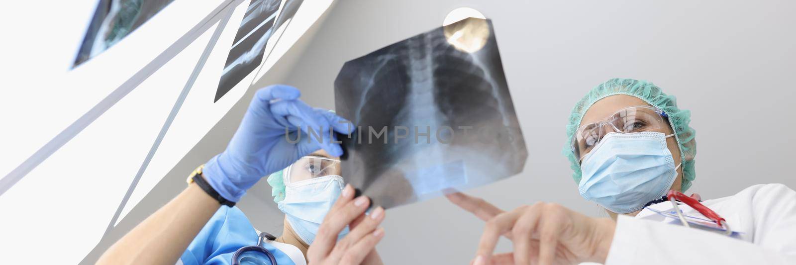 Doctors in medical gowns examine x ray of patient lungs in clinic by kuprevich