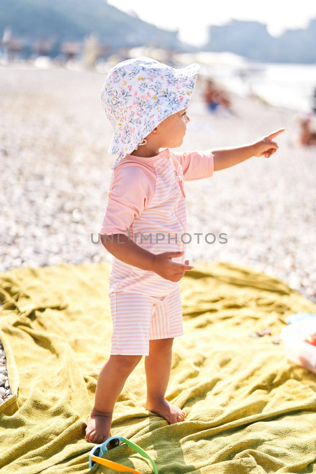 Little girl in a panama hat stands on the beach, pointing her finger into the distance. High quality photo