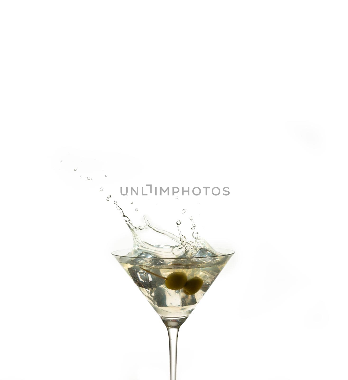 detail of a cocktail glass with an alcoholic preparation of ice and olives. Splash of an ice inside a crystal glass on a white background. drink concept. copy espace.